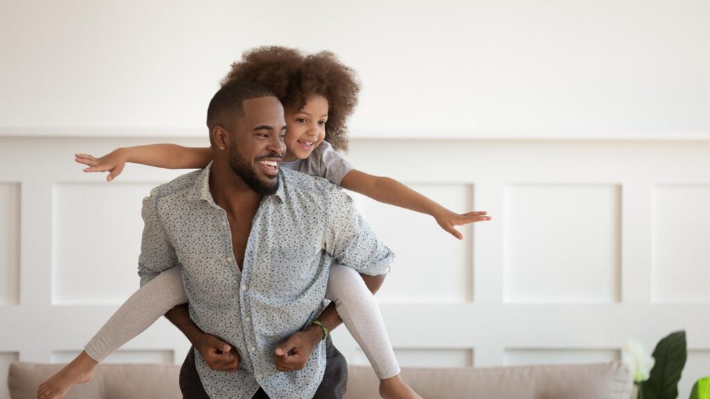 Handsome black man gives his adorable daughter a piggyback ride