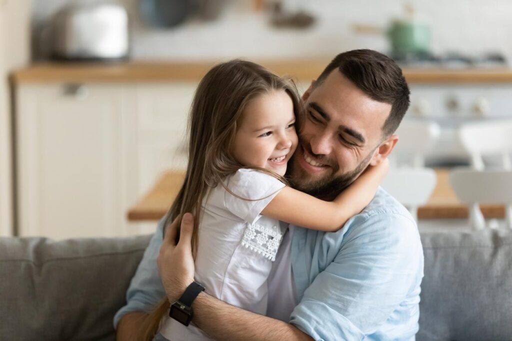 Cute little girl sits with her dad as they give each other a big hug