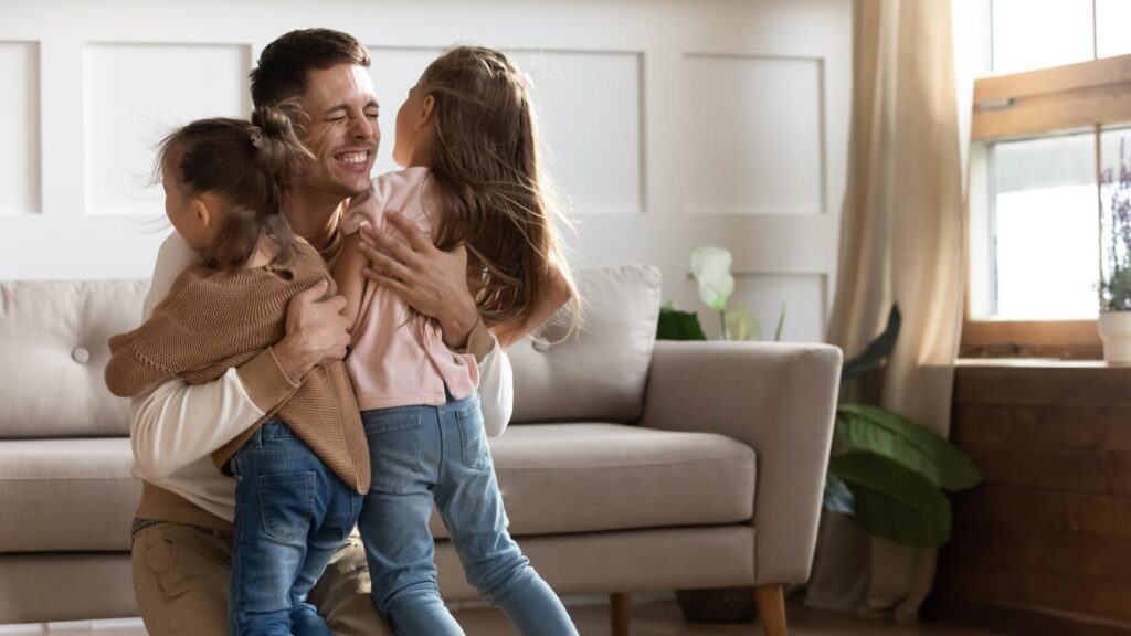 Two small girls hug their dad as he hugs them both in his arms